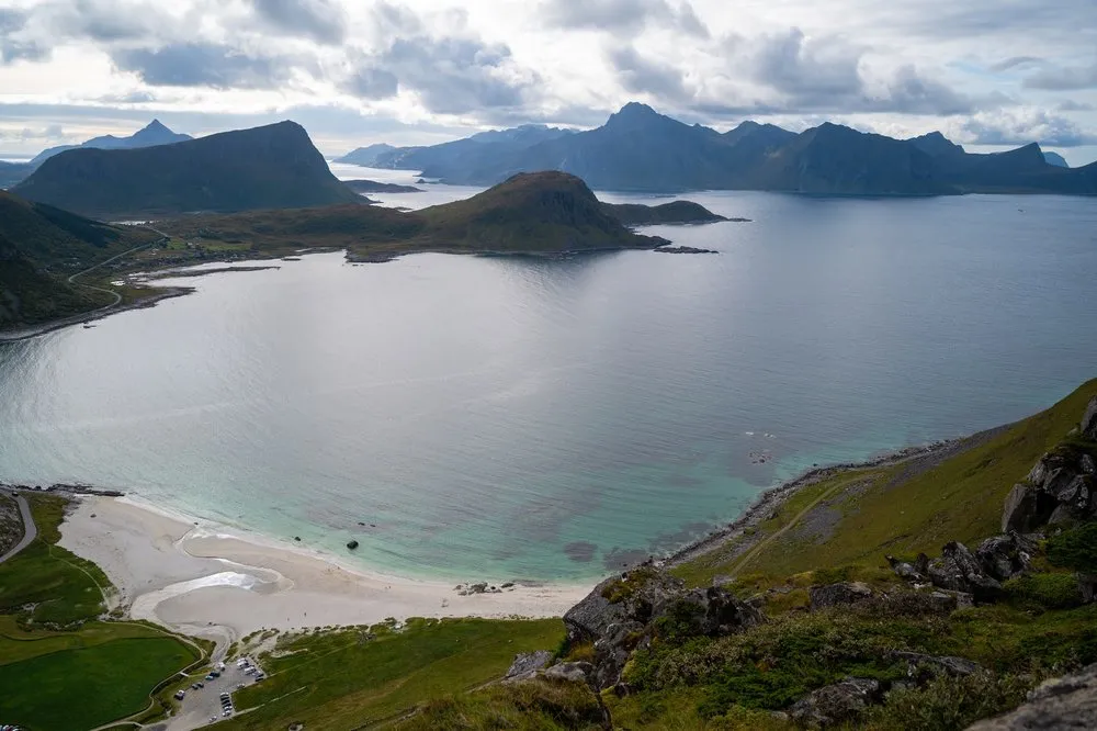 Die Bucht mit türkisem Wasser und hellem Sandstrand, am unteren Rand der Parkplatz