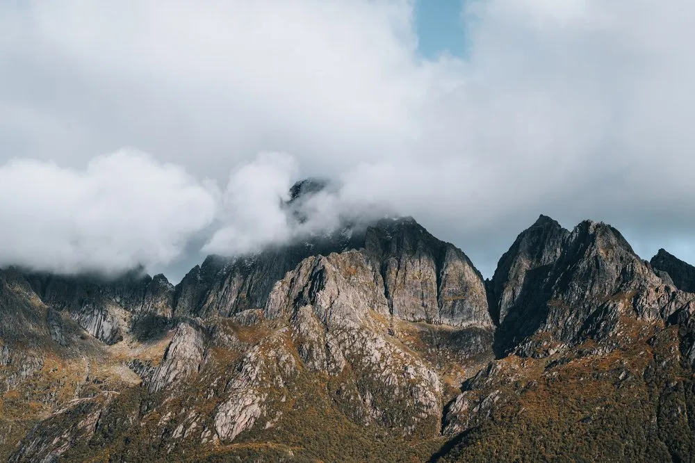 Felsige Berggipfel in warmem Herbstlicht, die Spitzen hängen in Wolken