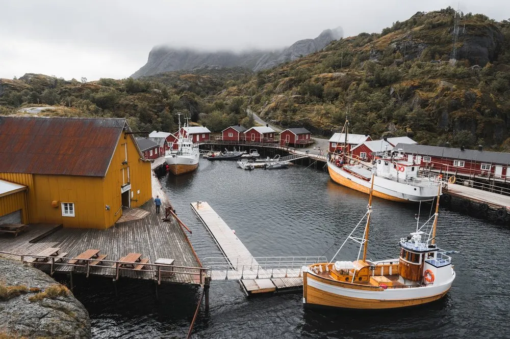 View from above of the harbour of Nusfjord with a yellow wooden house, red rorbuer and several wooden boats