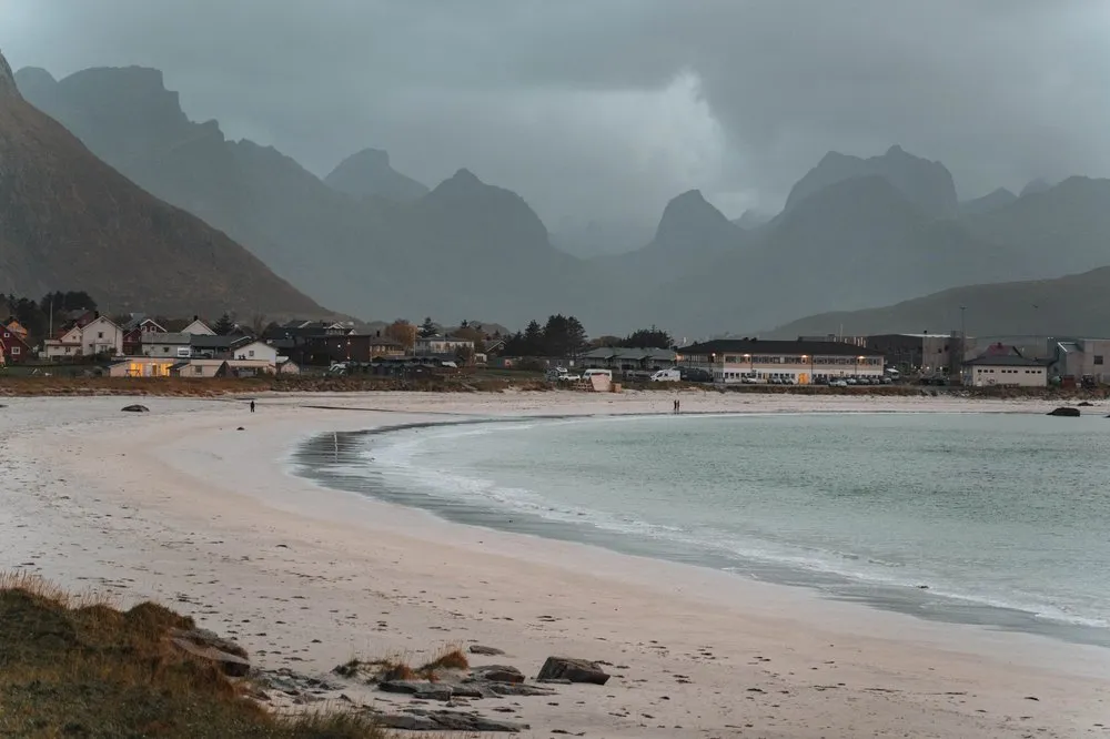 Der geschwungene Sandstrand von Ramberg, dahinter die Häuser des Dorfes vor dunklen Bergen