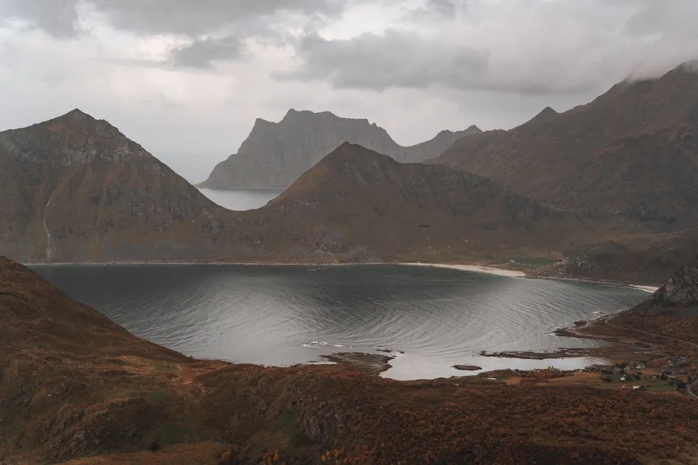 Blick vom Offersøykammen auf eine Bucht mit hellem Sandstrand, dahinter spitze Berge unter tiefen Wolken