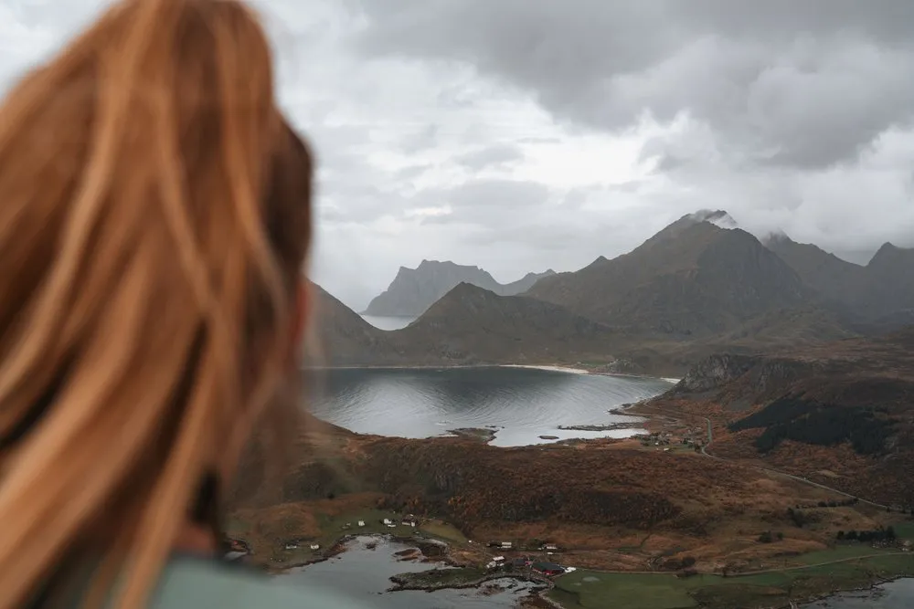 Eine Wanderin mit langen Haaren schaut vom Offersøykammen hinunter auf die Bucht, die Häuser am Ufer und die Berge