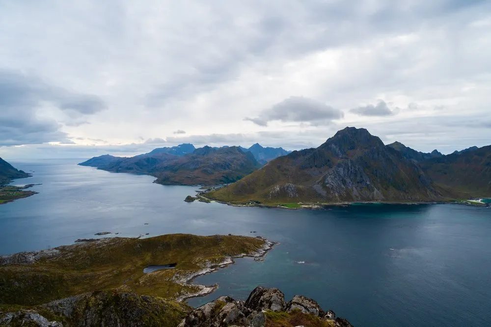 Ausblick über einen dunkelblauen Fjord auf ein Bergmassiv unter bewölktem Himmel