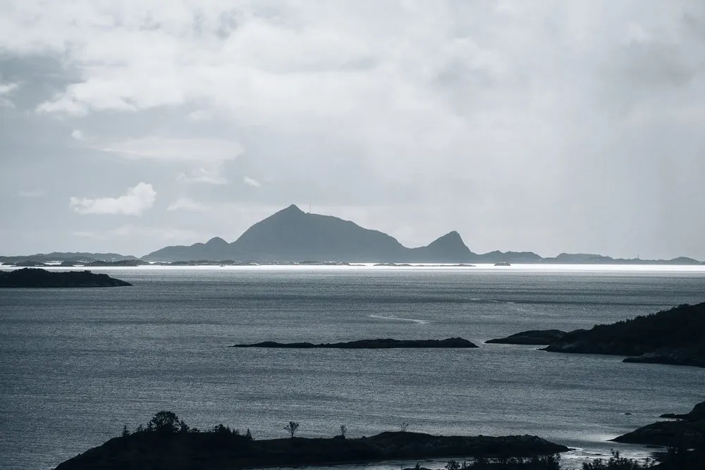 Silhouette einer bergigen Insel am Horizont über dem Meer, davor dunkle Felsinseln im Wasser