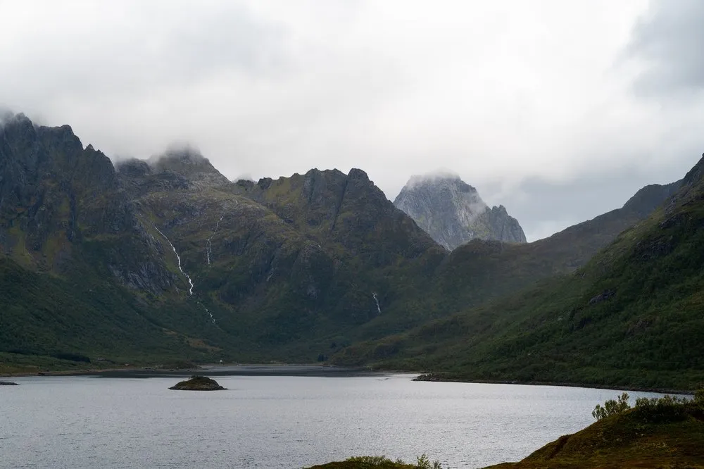 Berge mit dünnen Wasserfällen über einer Meeresbucht, im Wasser eine kleine Insel