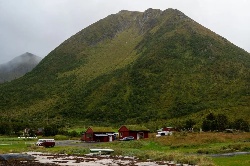 Der Campingplatz in Rystad mit roten Häuschen mit Grasdach am Fuss eines grünen Bergs, links ein VW-Bus