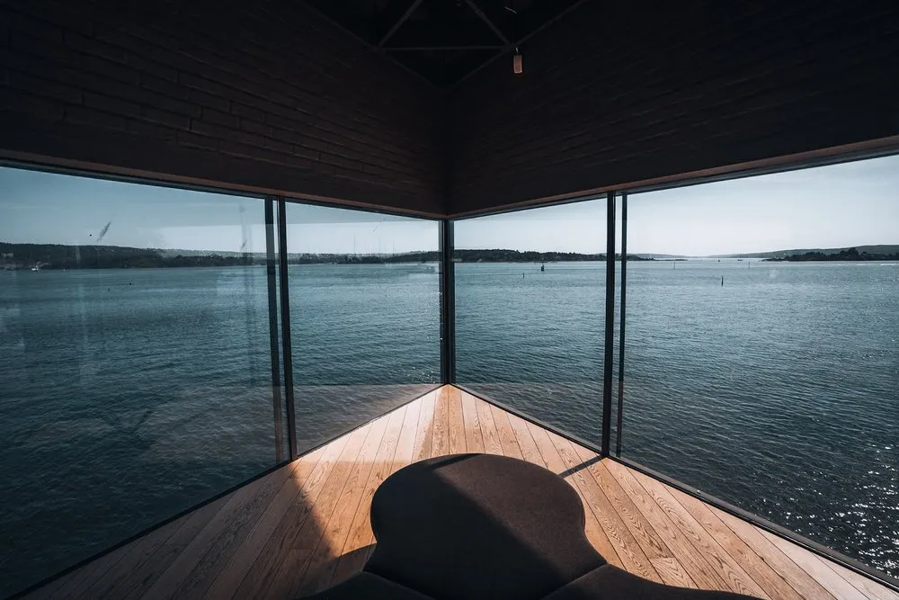 Blick aus dem Eckfenster des Maritim Museums über das Wasser, im Vordergrund ein runder dunkler Sitz auf hellem Holzboden
