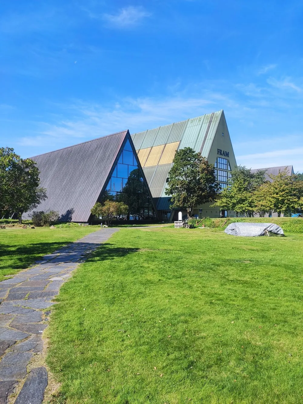 Das Fram Museum mit dem dreieckigen Dach und der Glasfront hinter einer Wiese, am Giebel steht FRAM