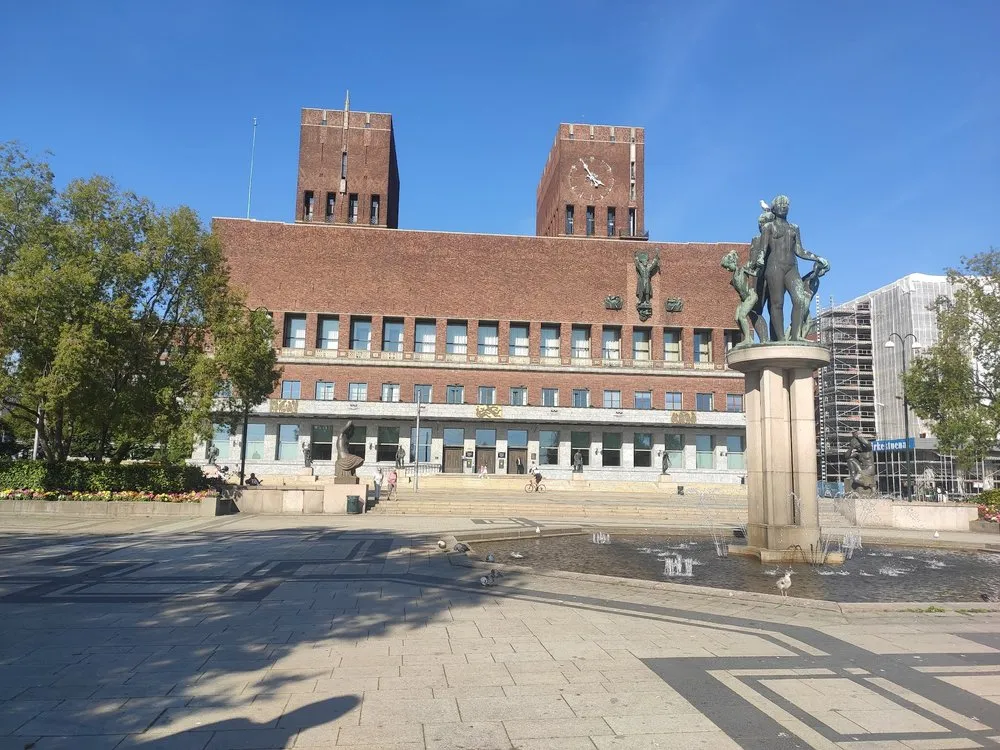 Das Rathaus mit zwei Backsteintürmen, davor ein Brunnen mit einer Bronzefigur auf einem Pfeiler und ein gepflasterter Platz