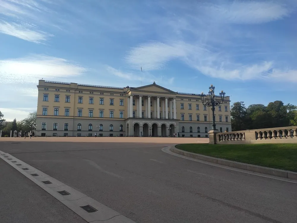 Das Königliche Schloss mit heller Fassade und Säulenportikus hinter einem grossen Vorplatz, rechts eine Laterne und eine Balustrade