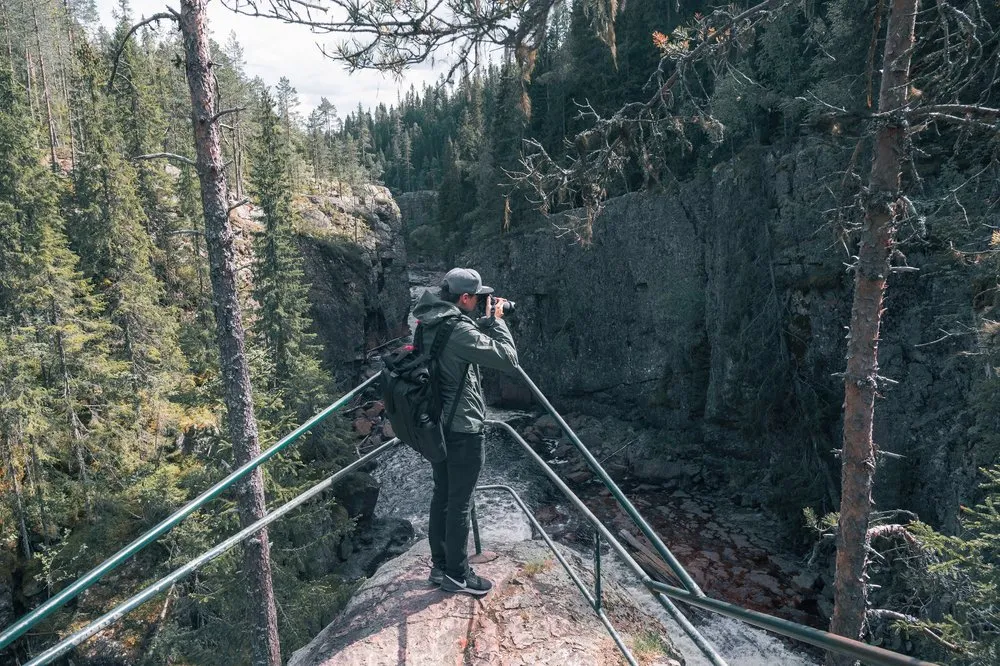 Nicolas fotografiert von einem Felsvorsprung mit Geländer in die Schlucht am Helvetesfallet
