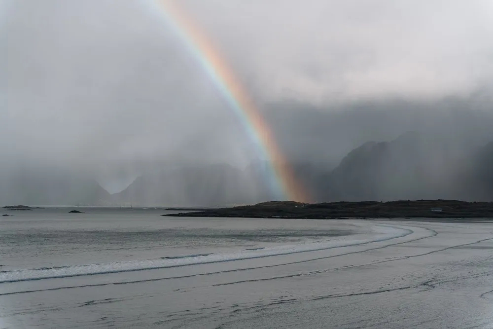Ein Regenbogen über dem Strand von Fredvang, dahinter Regenschauer über den Bergen