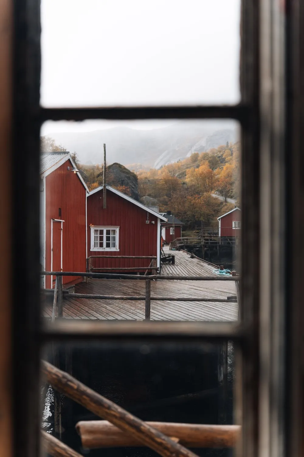 Durch ein altes Fenster auf die roten Häuser und den Steg von Nusfjord