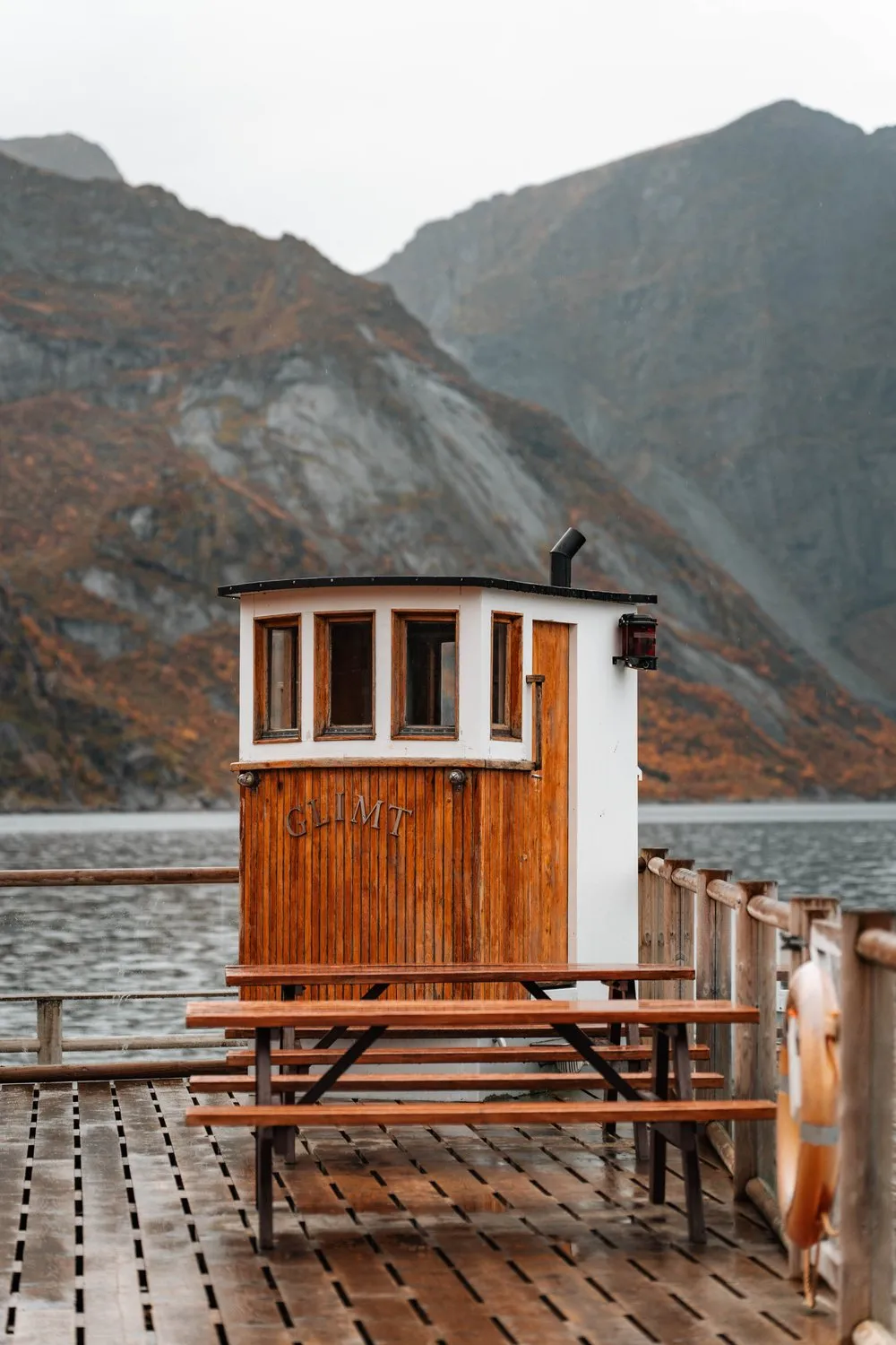 Das alte hölzerne Steuerhaus eines Bootes auf einem nassen Holzdeck in Sakrisøy, dahinter herbstliche Berge