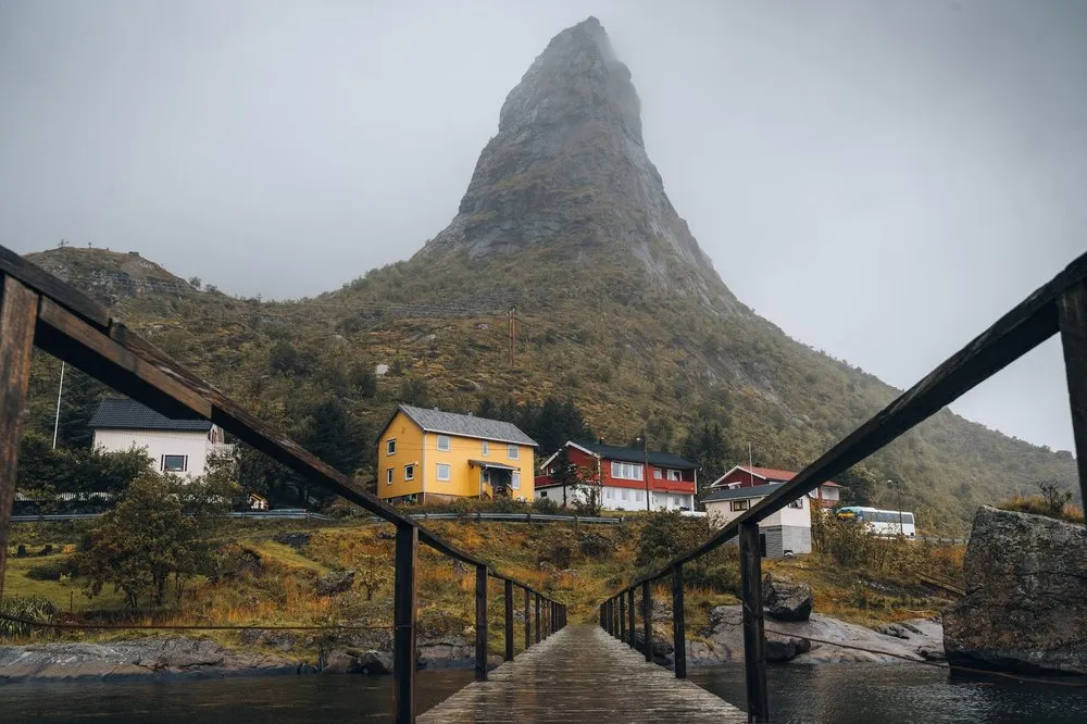 In Reine aus niedriger Perspektive über die nasse Holzbrücke gesehen, links und rechts das Geländer, dahinter der spitze Berg