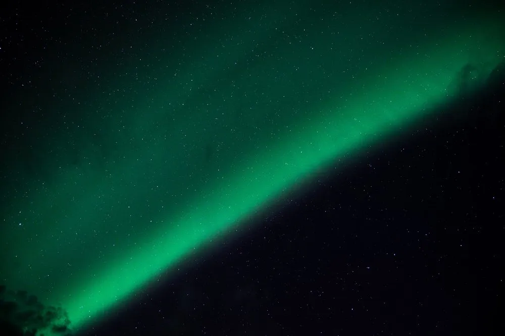 Ein breiter grüner Nordlichtstreifen zieht sich diagonal über den Sternenhimmel