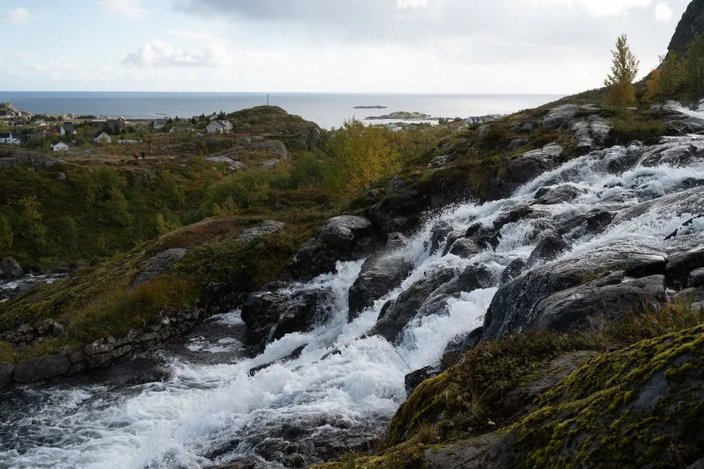Der Lofoten Wasserfall stürzt über Felsstufen, im Hintergrund Häuser und das Meer