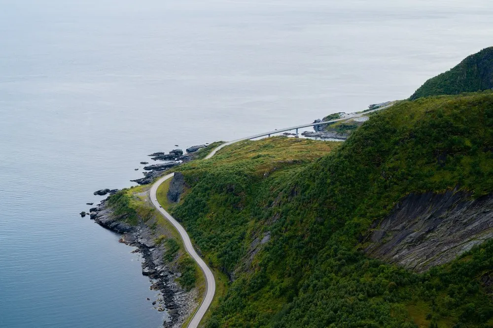 Eine Küstenstrasse windet sich zu einer Brücke, links das ruhige Meer, rechts ein bewachsener Steilhang