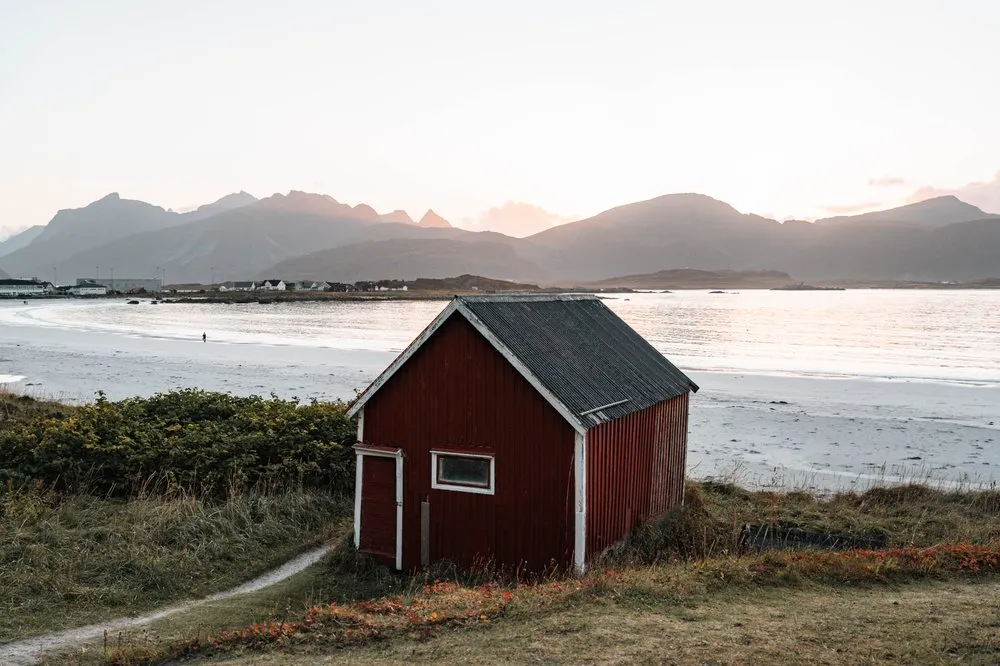 Das rote Häuschen über dem Rambergstranda, dahinter der helle Strand und die Berge im Abendlicht