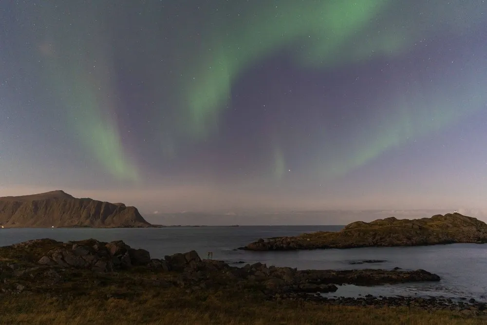 Grüne Nordlichtbänder am Sternenhimmel über den Felsen und dem Meer