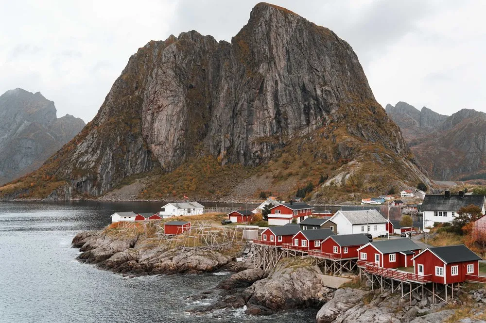 Die roten Rorbuer von Hamnøy auf Stelzen über den Felsen, dahinter der steile graue Felsberg, von der Brücke aus