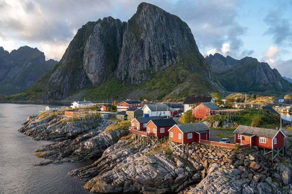 Die Fischerhäuschen von Hamnøy in warmem Licht, dahinter der Bergstock mit Wolken am Himmel