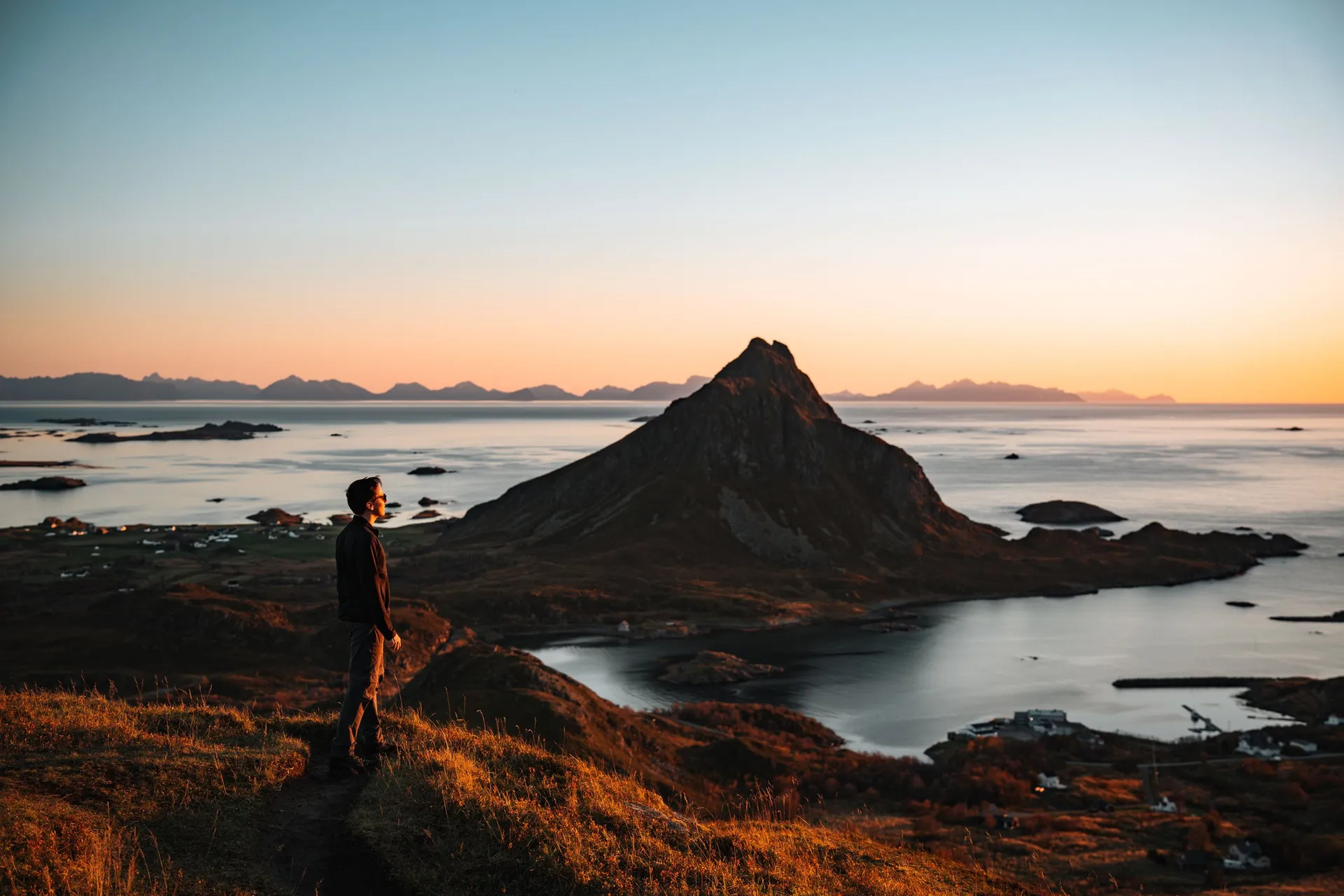 Nicolas steht im Abendlicht am Hang, vor ihm der spitze Gullstabben über der Bucht Krumsvågen, am Horizont die Berge der Lofoten