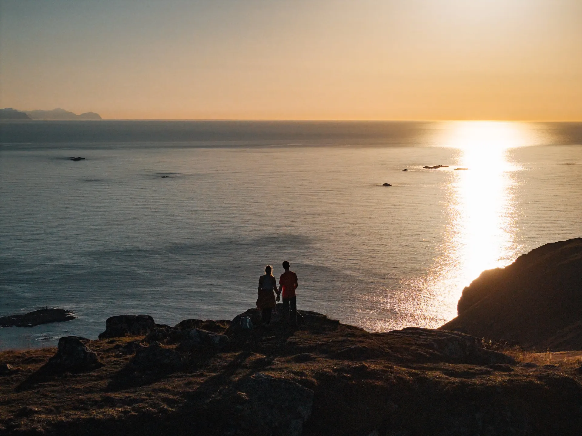 Unsere Silhouetten Hand in Hand auf dem Skårvågsfjellet, vor uns spiegelt sich die Sonne im Meer