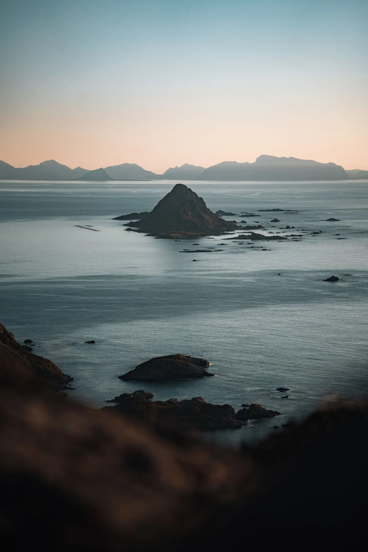 Die spitze Insel Gaukværøya im ruhigen Meer, dahinter am Horizont die Berge der Lofoten, vom Skårvågsfjellet aus