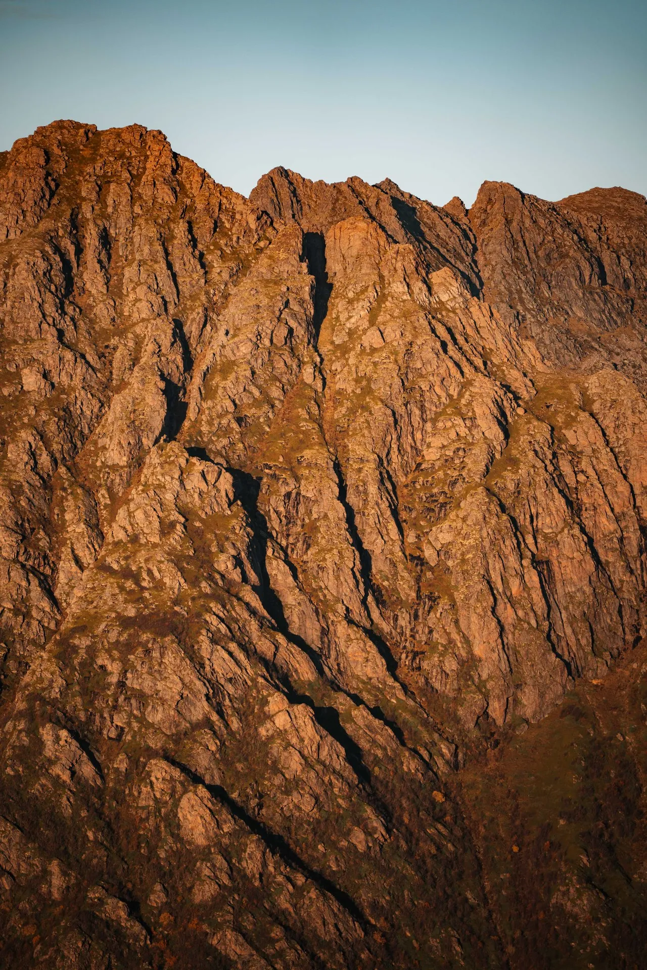 Zerklüftete Felsen leuchten rotbraun im Abendlicht, vom Skårvågsfjellet aus