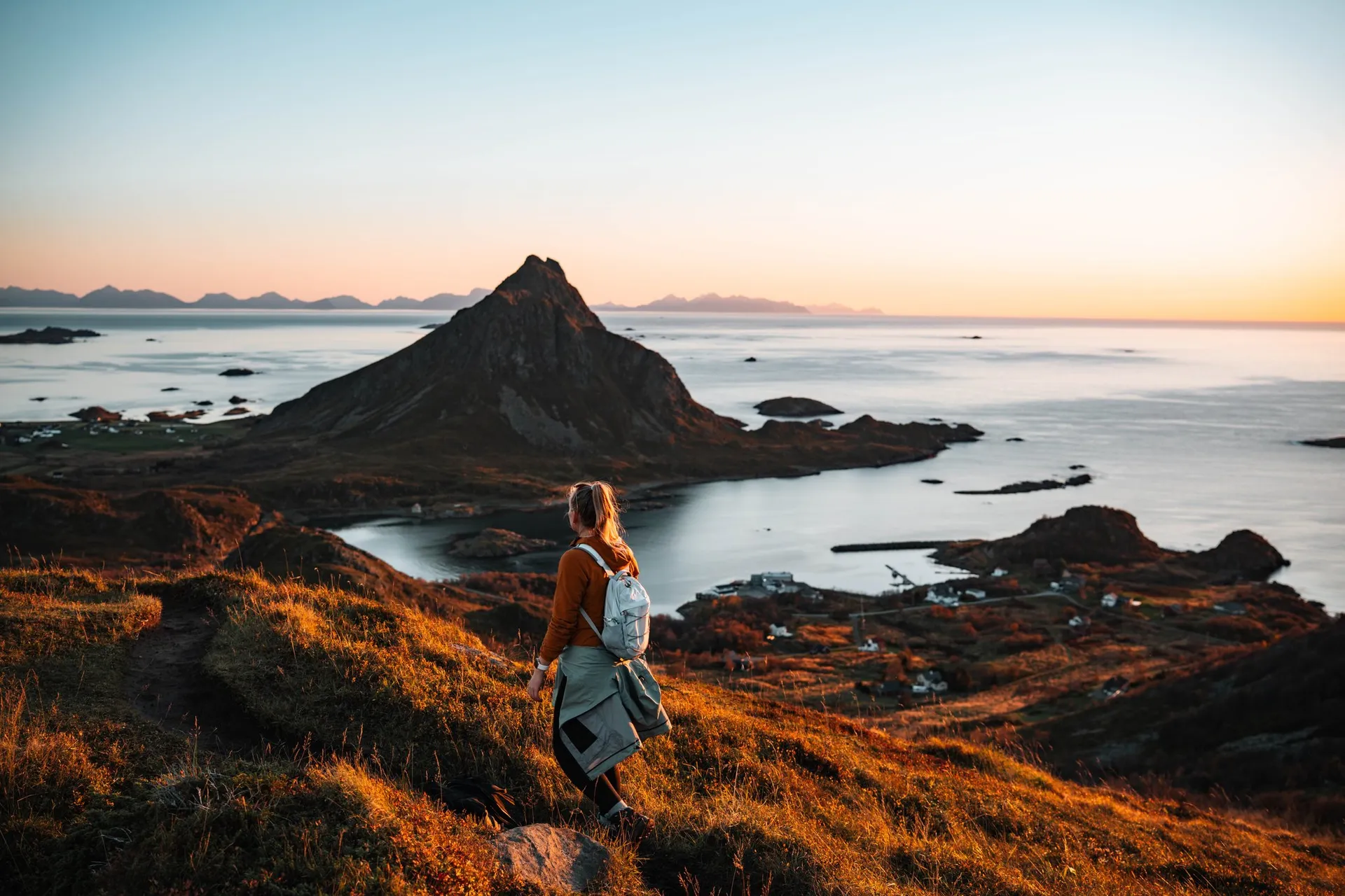 Annina mit Rucksack auf dem Weg hinunter, vor ihr der spitze Gullstabben über der Bucht Krumsvågen, am Horizont die Lofoten