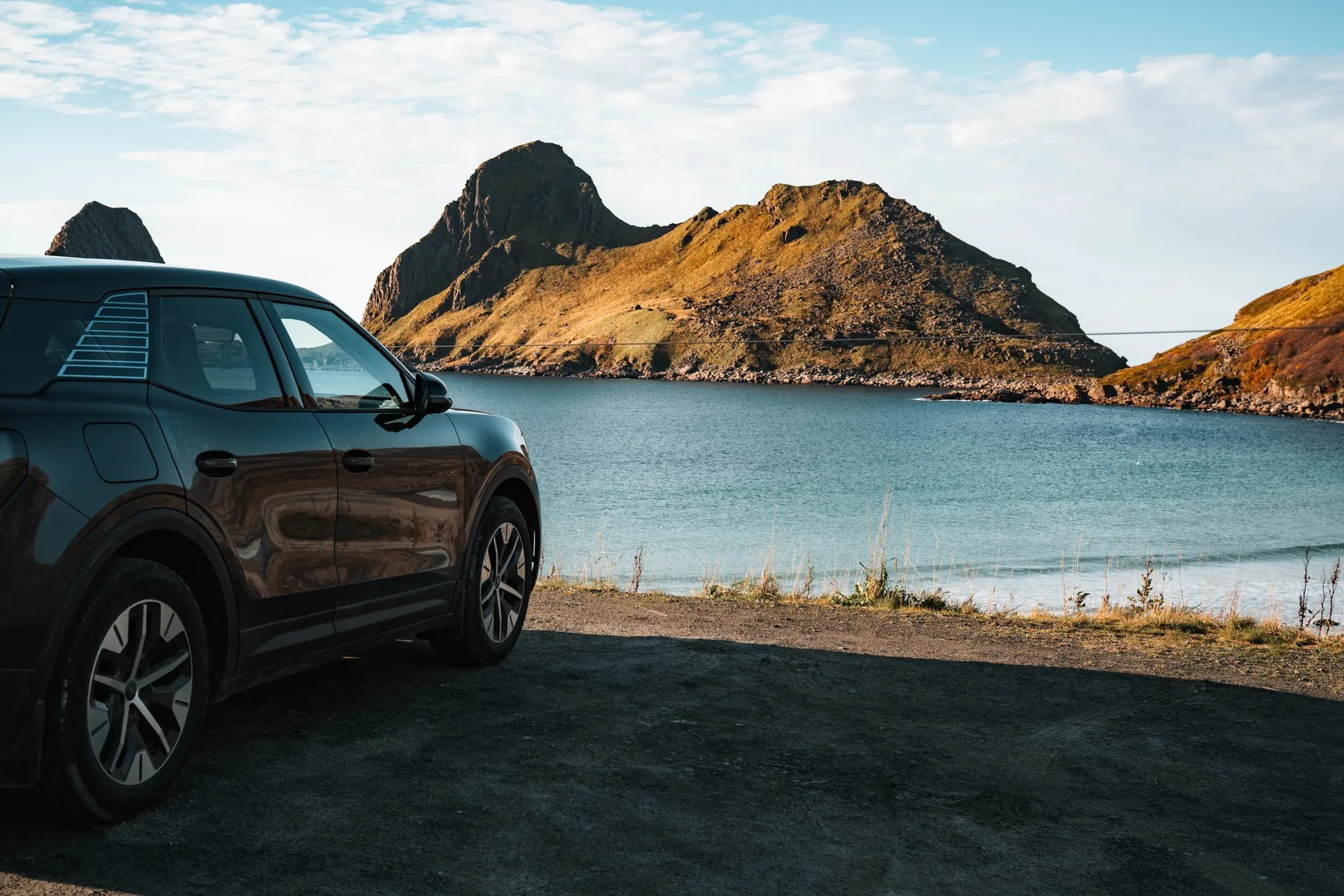 Unser Mietauto am Rand der Bucht von Sandvika, dahinter die Felshalbinsel Engenyken im Sonnenlicht