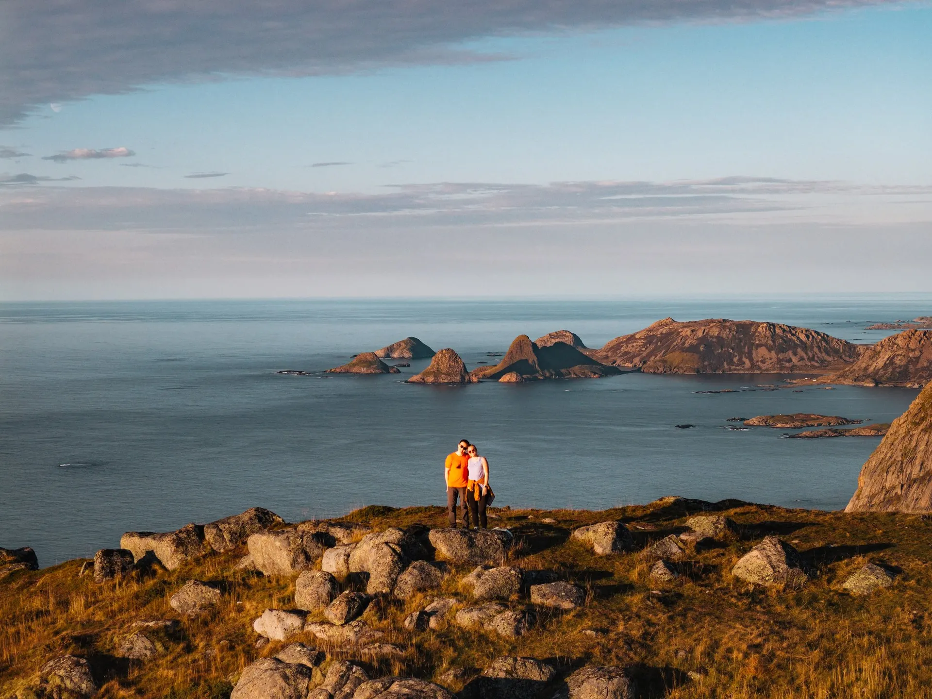 Wir beide auf dem felsigen Gipfel des Skårvågsfjellet, dahinter Felsinseln und das Meer im Abendlicht