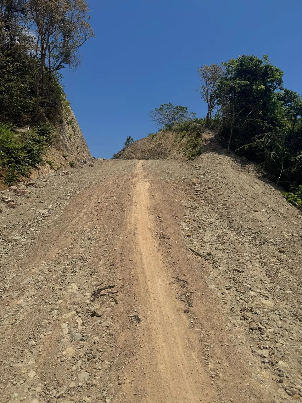 A steep dirt path with gravel winds up the slope between embankments, blue sky above