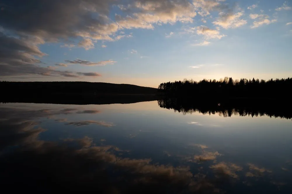 Sonnenuntergang über dem See, die dunklen Ufer und die Wolken im Abendlicht spiegeln sich im Wasser