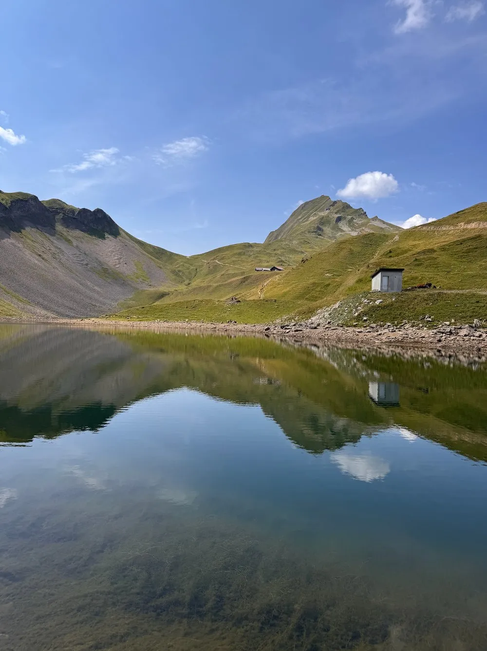 Der Eisee spiegelt Berge und Wolken, am Ufer steht eine kleine Hütte