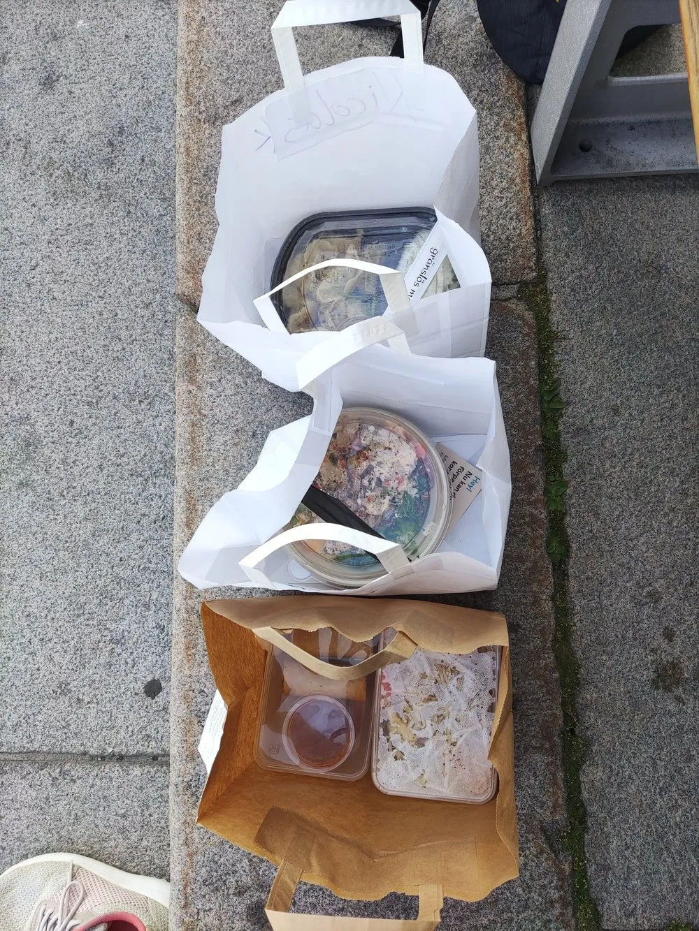 Drei Papiertüten mit Take-Away-Essen nebeneinander auf dem Steinpflaster, zwei weisse und eine braune