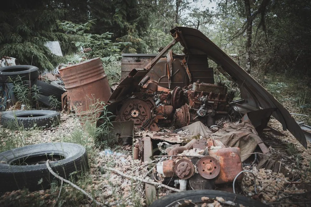 Rostige Motorteile, Reifen und ein Fass liegen verstreut am Waldboden
