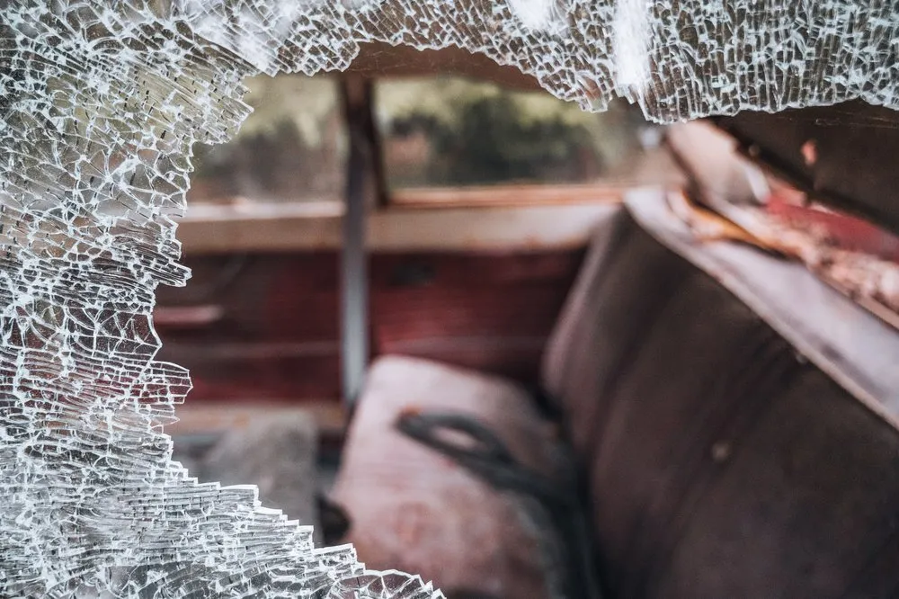 Zersplittertes Glas im Vordergrund, dahinter unscharf ein Autositz im rötlichen Innenraum