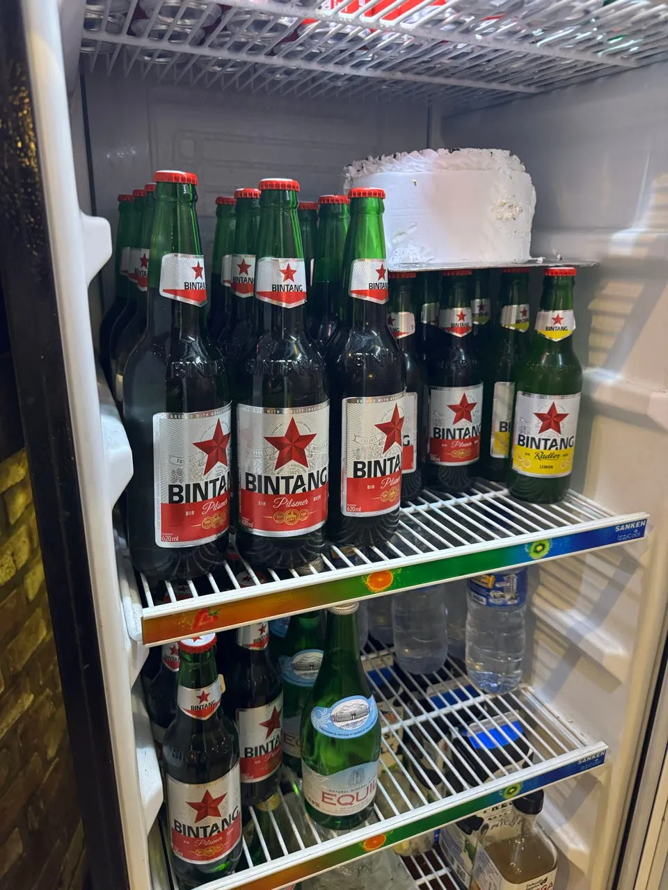 Kühlschrank mit Flaschen der Biermarke Bintang und Wasserflaschen, obendrauf eine weisse Torte
