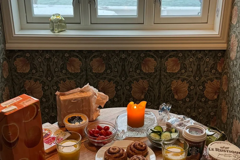 Gedeckter Frühstückstisch mit Zimtschnecken am Fenster, draussen der Fjord