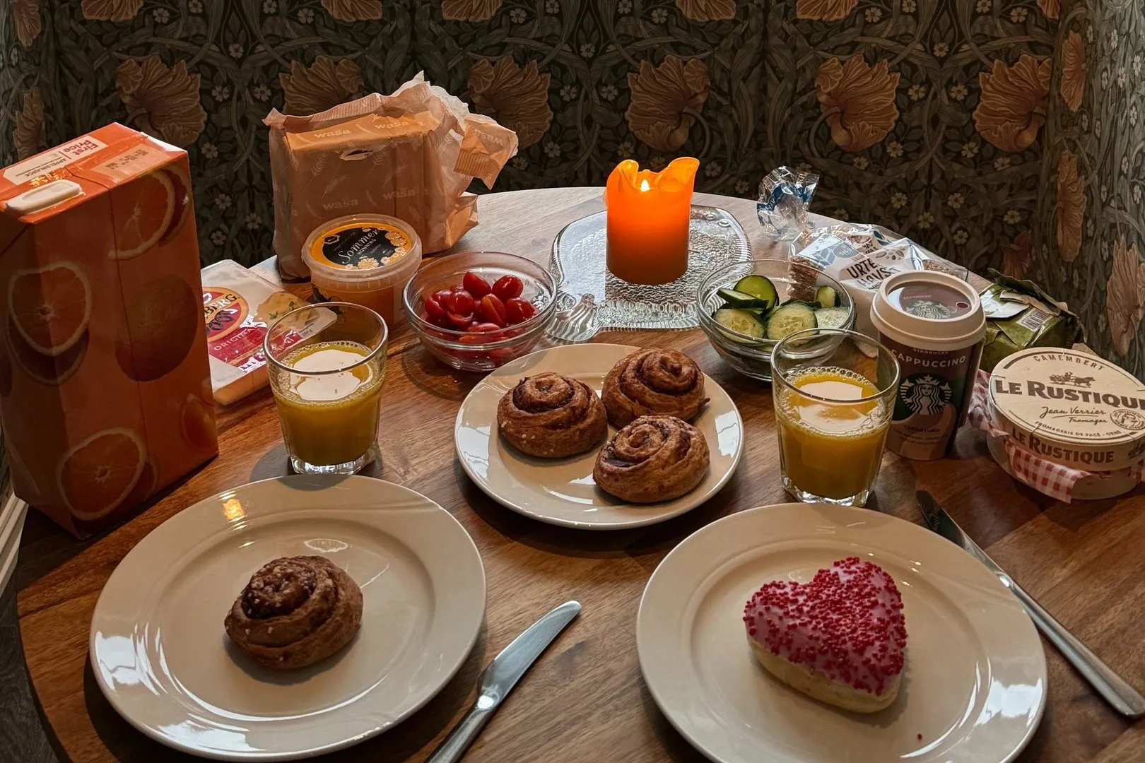 Gedeckter Frühstückstisch mit Kerze, Zimtschnecken, Cherrytomaten und Orangensaft