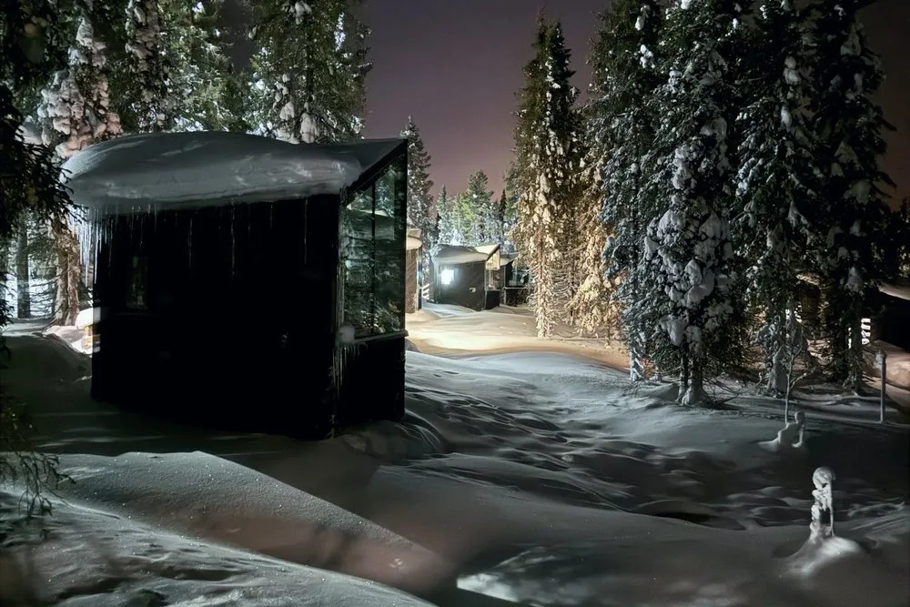 Das Glas-Iglu im nächtlichen Wald, darüber schwache Nordlichter