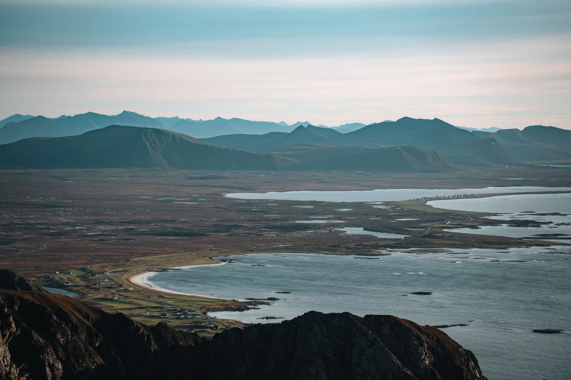 A wide plain with lakes and a long pale beach, mountains behind, seen from Måtind