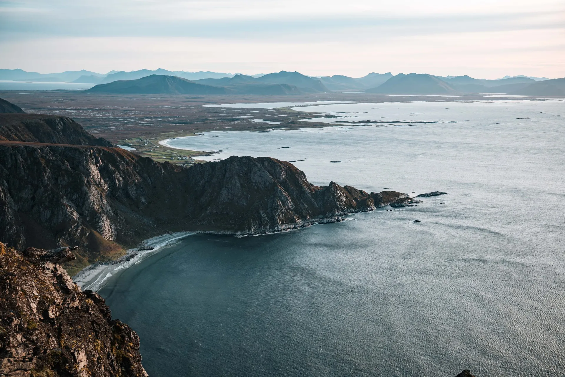 Rocky cliffs run down to a bay with a pale beach, seen from Måtind