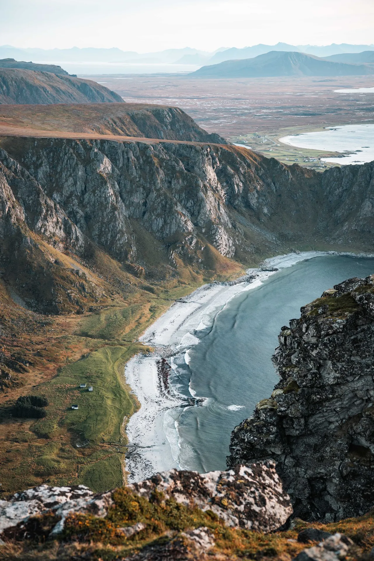 Far below steep rock walls lies a bay with a pale beach, seen from Måtind