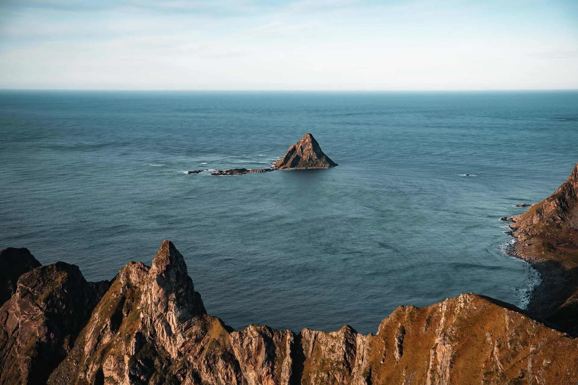 The triangular bird island of Bleiksøya in the sea, a jagged rock ridge in front, seen from Måtind
