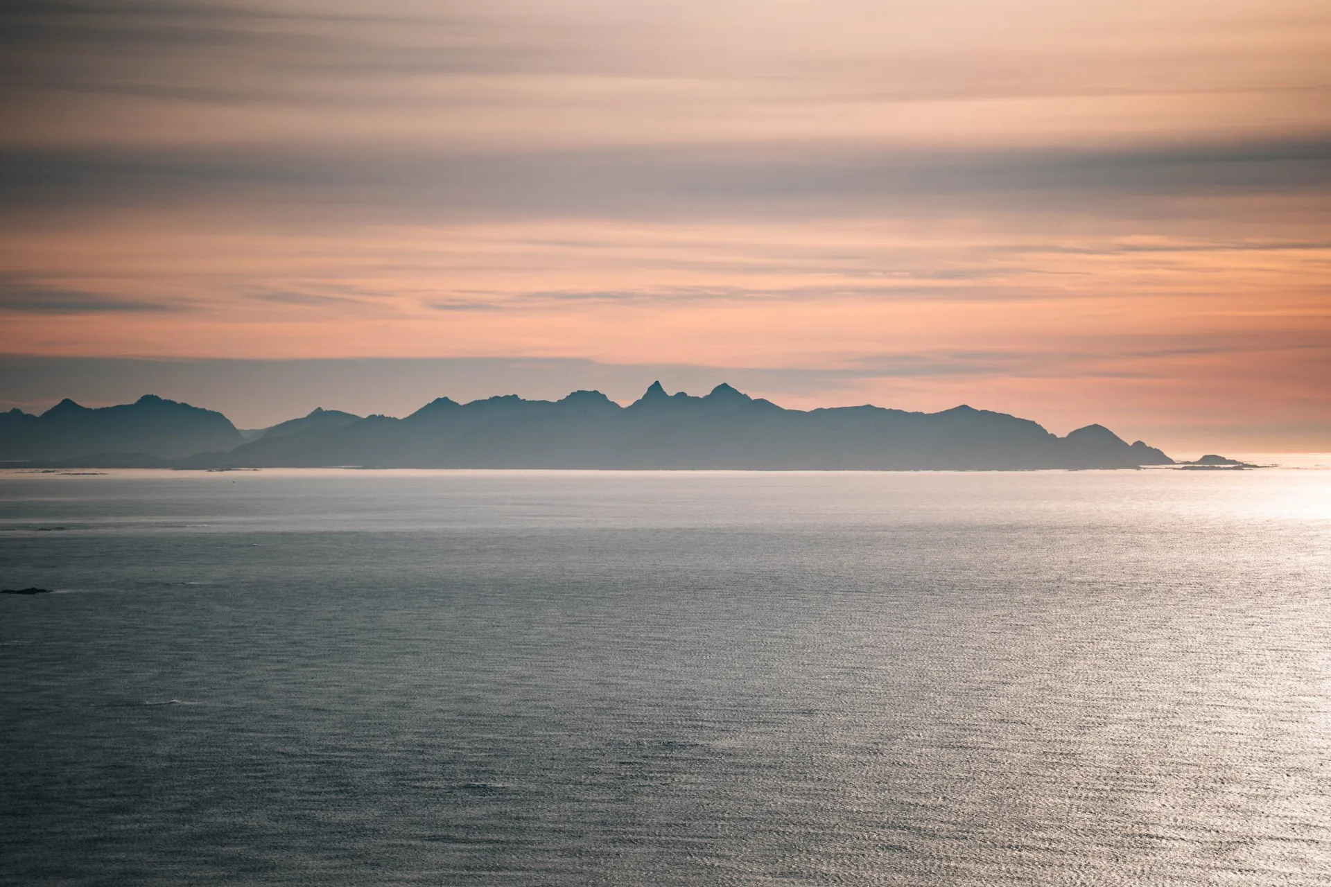 A band of jagged mountains on the horizon under pink evening clouds, seen from Måtind