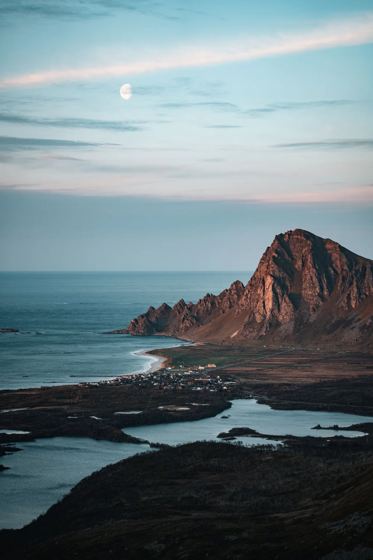 The moon above a reddish lit mountain by the sea, on the way down Måtind