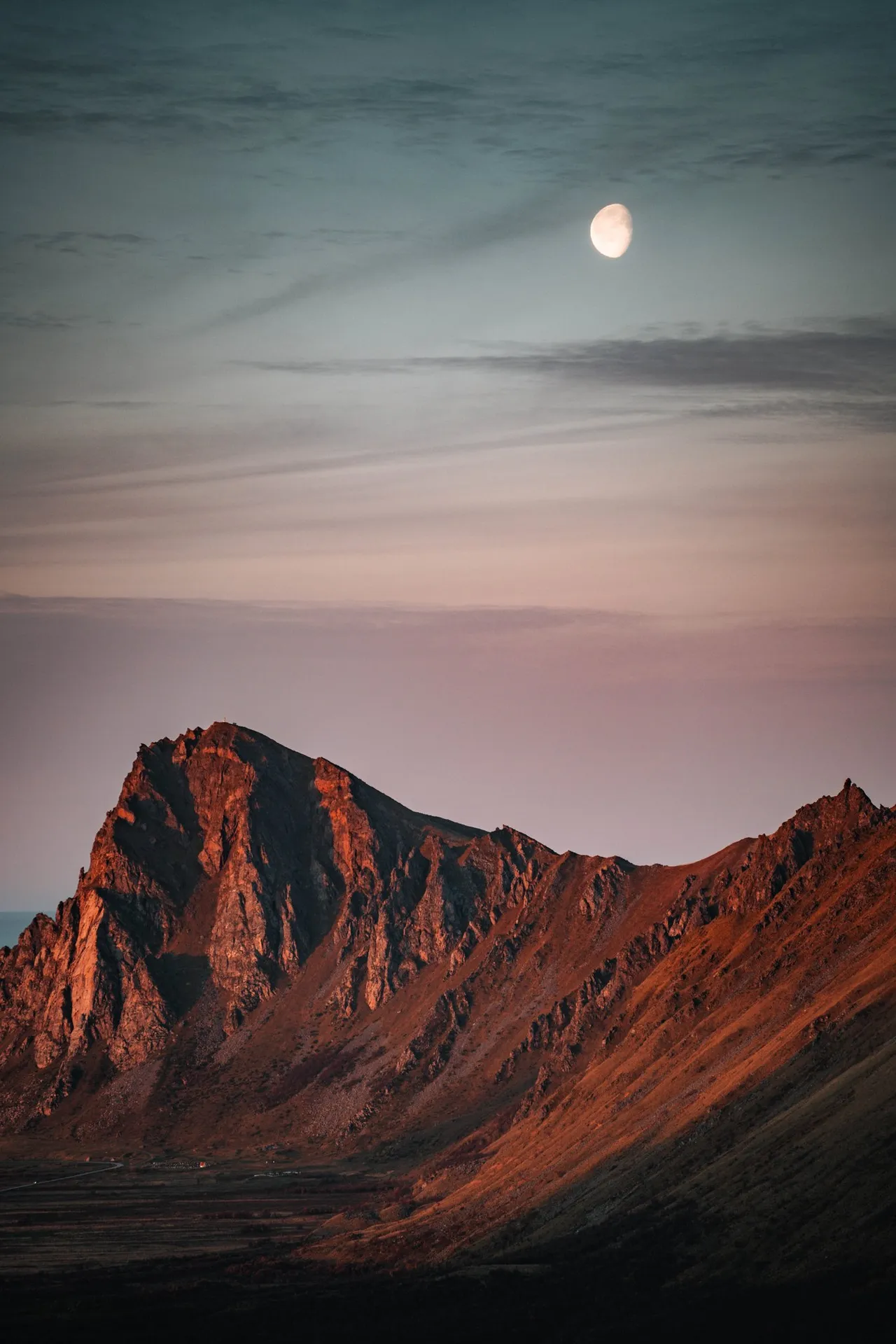 The moon in the pink sky above a mountain in the last light, on the way down Måtind